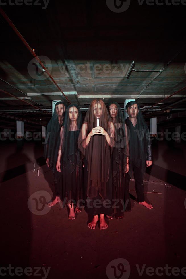 uma grupo do diabo adoradores dentro todos Preto roupas e transparente véus segurando velas juntos durante uma adoração ritual dentro uma construção foto