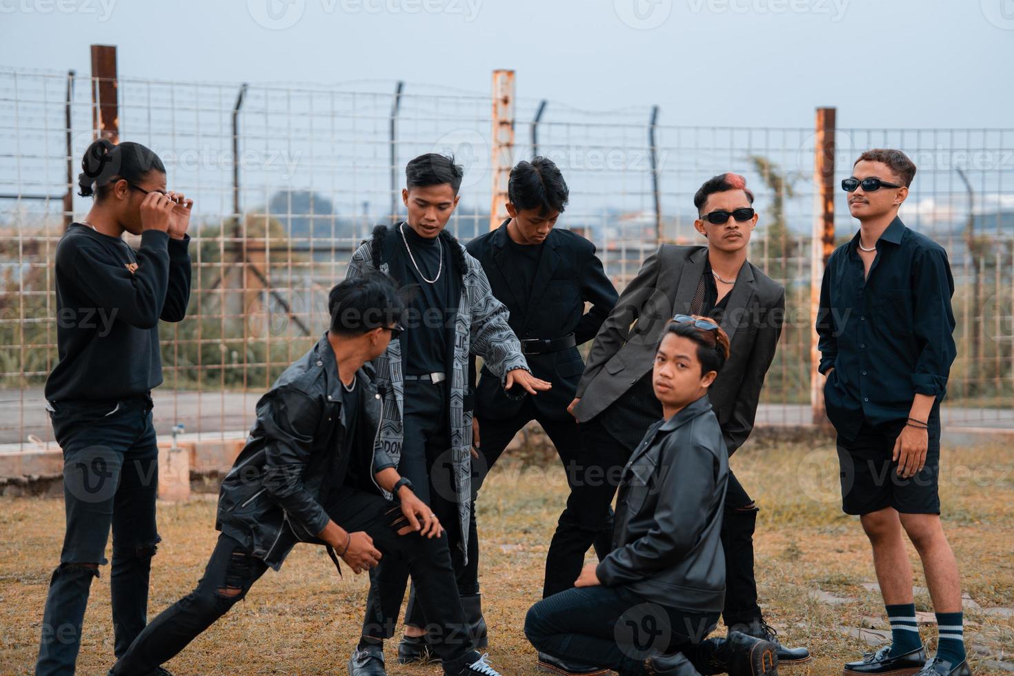 uma grupo do Adolescência Rapazes dentro Preto roupas posando muito galantemente com seus amigos dentro uma campo foto