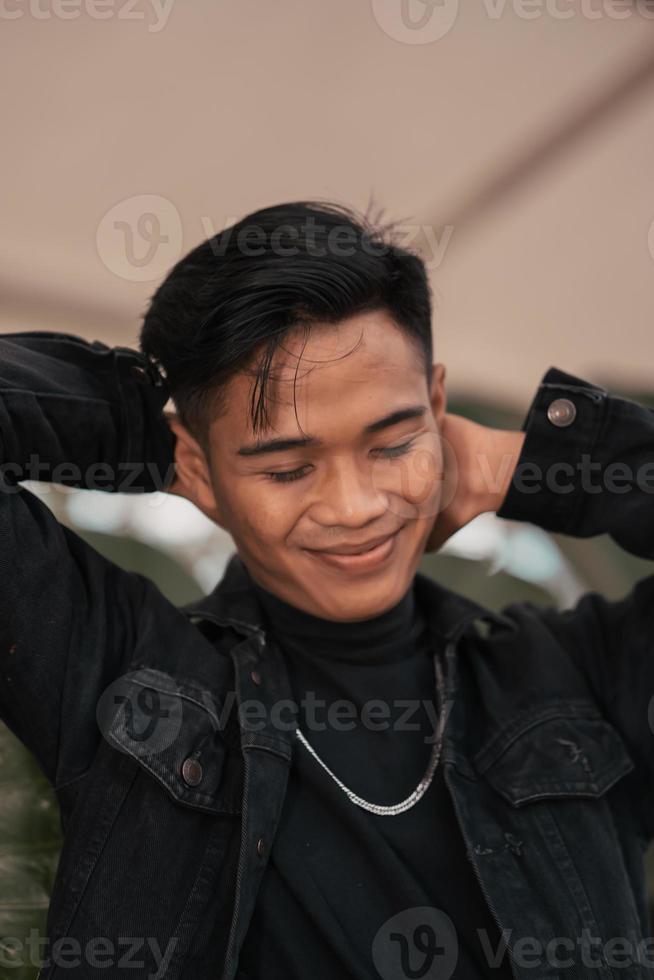 a ásia homem dentro uma Preto jeans Jaqueta posando com uma alegre face e muito bonito dentro uma cafeteria foto