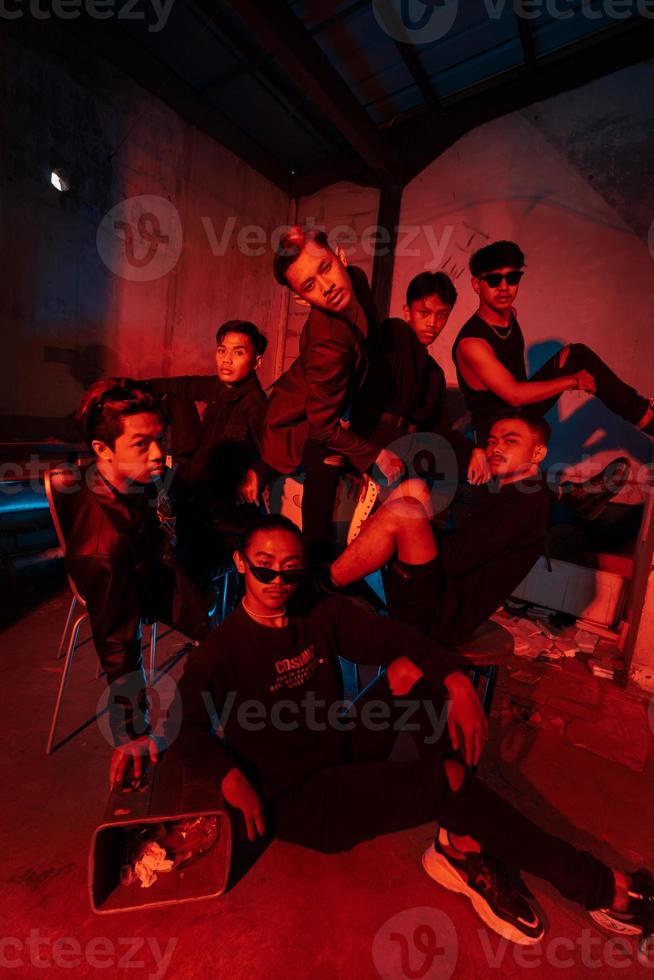 uma grupo do ásia adolescentes dentro Preto roupas posando muito danadinho com seus amigos dentro uma armazém com uma vermelho luz foto