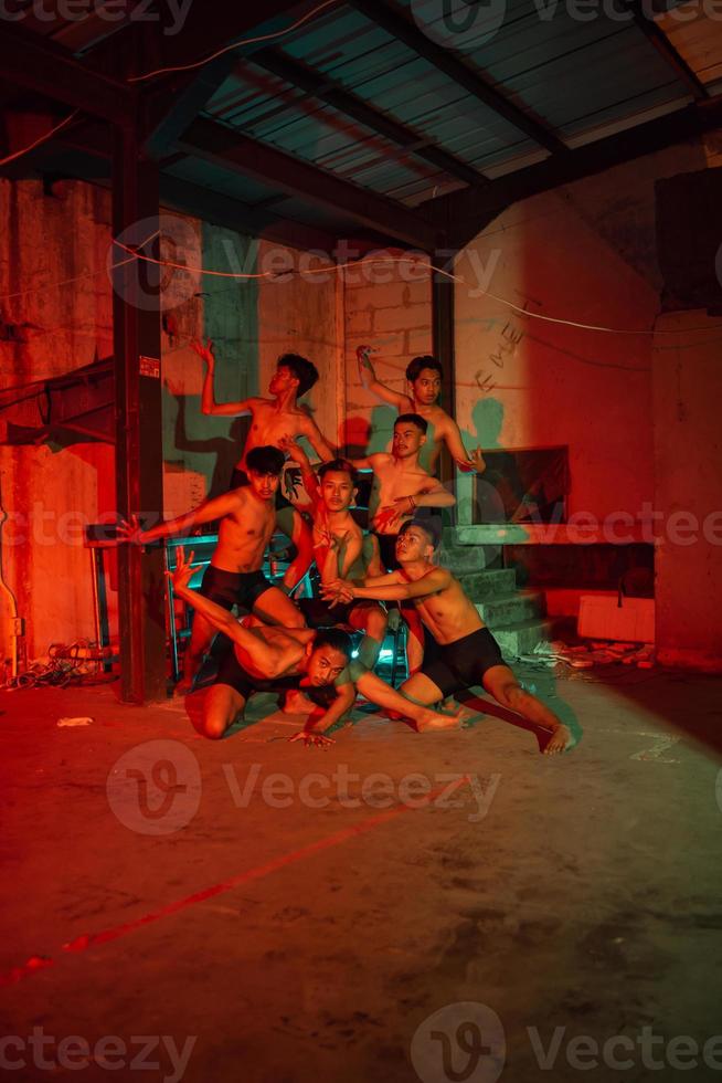 uma grupo do homens sem roupas dançando poses dentro a velho construção com uma vermelho luz foto