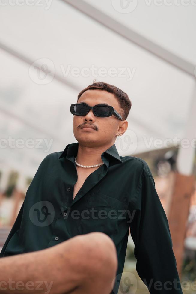 a ásia homem com uma bigode face vestindo uma camisa e oculos de sol dentro uma muito masculino estilo foto