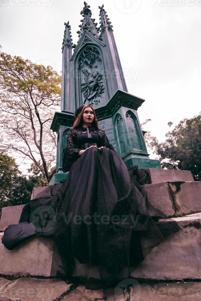 a ásia mulher vestido todos dentro Preto estava sentado dentro uma cemitério com uma muito assustador expressão enquanto atendendo a morte do dela irmão foto