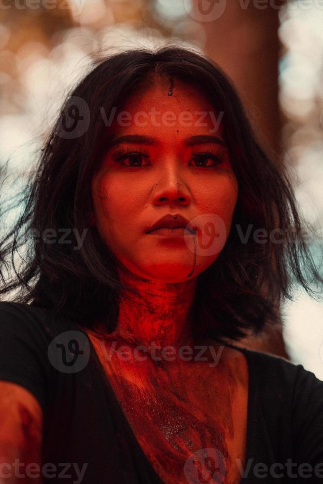 uma fêmea serial assassino dentro Preto roupas e coberto dentro sangue tem uma assustador face sentado dentro a meio do uma floresta foto