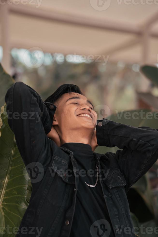 a ásia homem dentro uma Preto jeans Jaqueta posando com uma alegre face e muito bonito dentro uma cafeteria foto