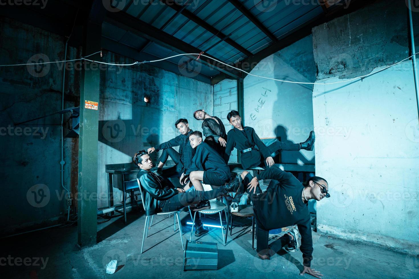 uma grupo do ásia adolescentes dentro Preto roupas posando muito friamente enquanto sentado dentro uma armazém cadeira que é aceso azul foto