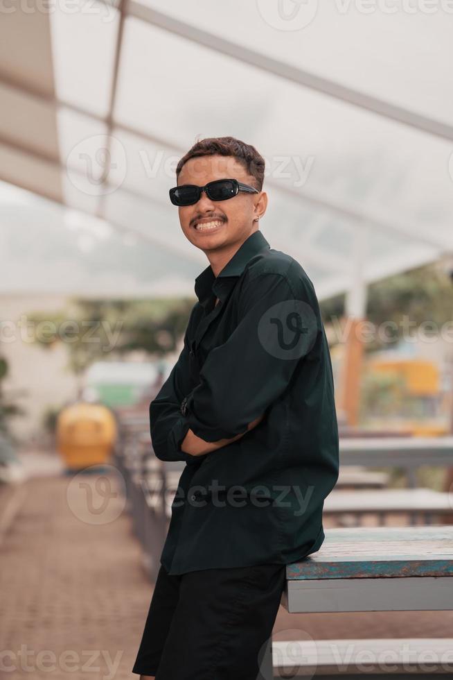 a ásia homem com uma bigode face vestindo uma camisa e oculos de sol enquanto suspensão Fora com dele amigos dentro uma cafeteria foto