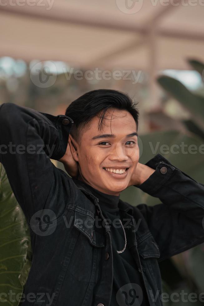 a ásia homem dentro uma Preto jeans Jaqueta posando com uma alegre face e muito bonito dentro uma cafeteria foto