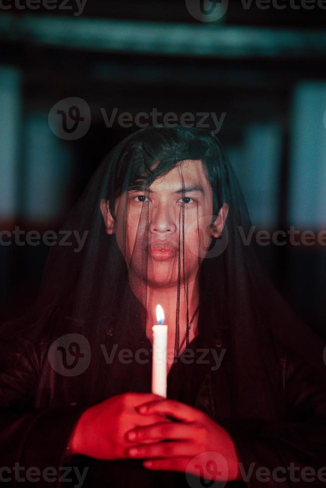 uma homem vestido todos dentro Preto segurando uma vela quando indo para uma cemitério para executar rituais foto