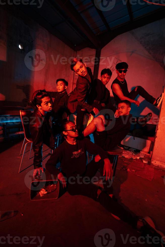 uma grupo do ásia adolescentes dentro Preto roupas posando muito danadinho com seus amigos dentro uma armazém com uma vermelho luz foto