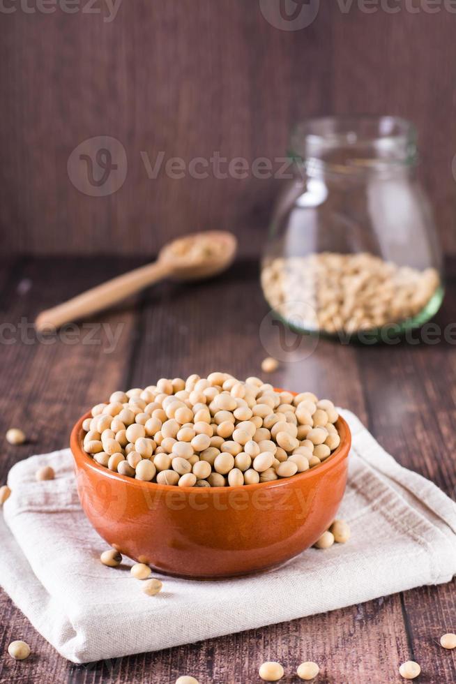 cru soja sementes dentro uma tigela, colher e jarra em a mesa. fonte do vegetal proteína. vertical Visão foto