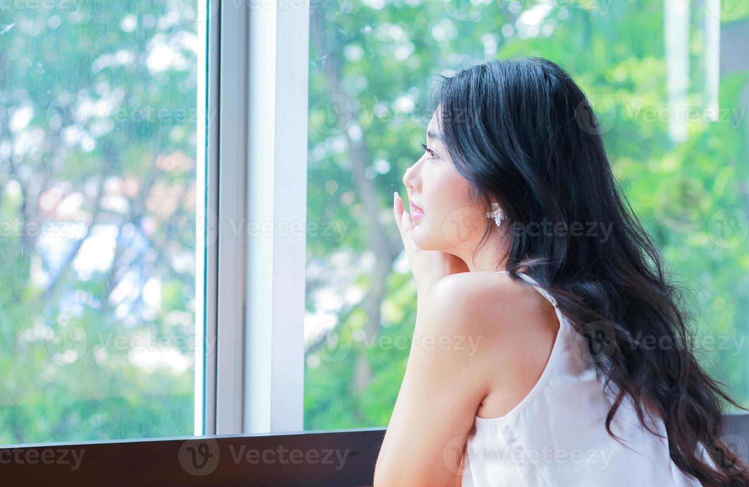 retrato de uma linda mulher asiática sentada alegremente perto da janela em fundo natural foto