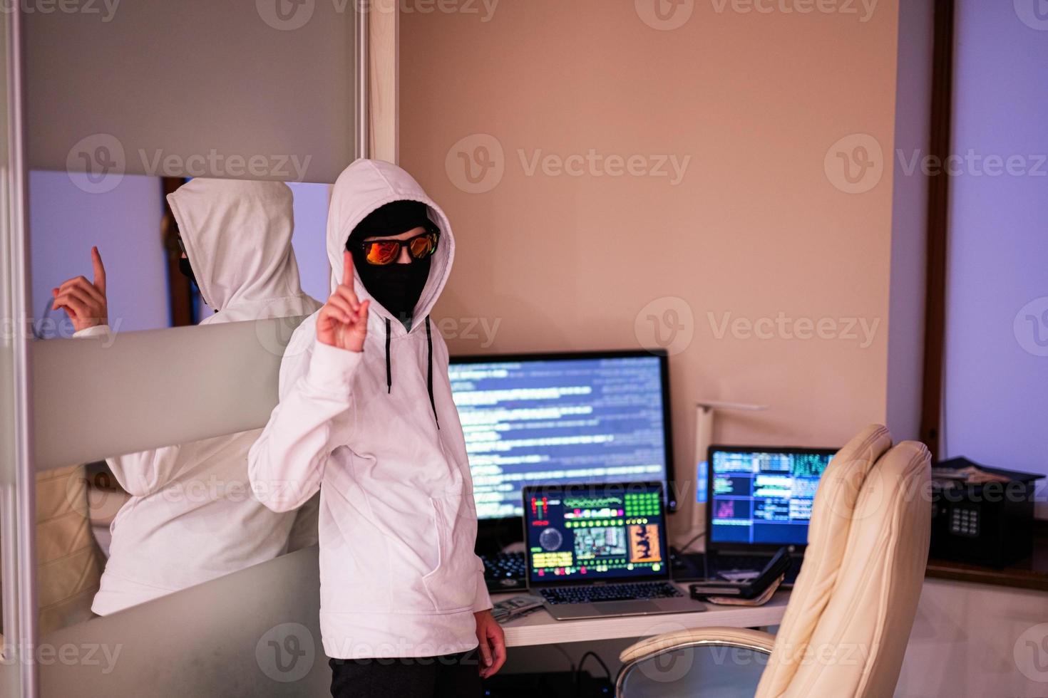 Garoto hacker mostrar dedo. Internet roubo . homem vestindo uma balaclava atrás uma computador portátil. foto