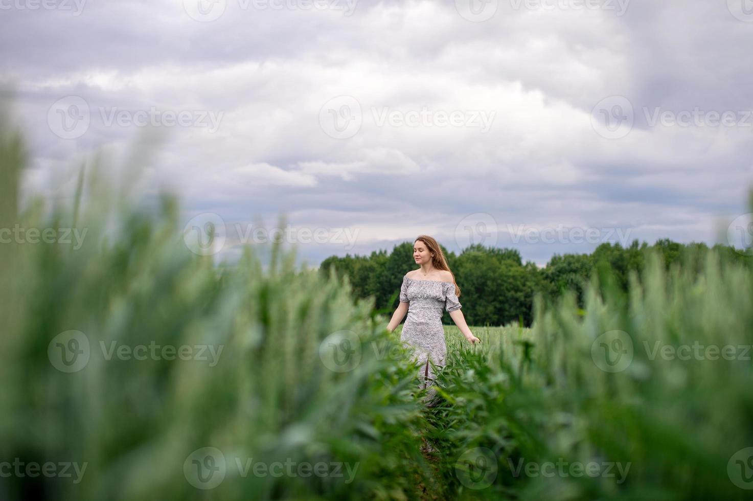 uma fofa menina com grandes cabelo dentro uma vestir corre através uma trigo campo foto