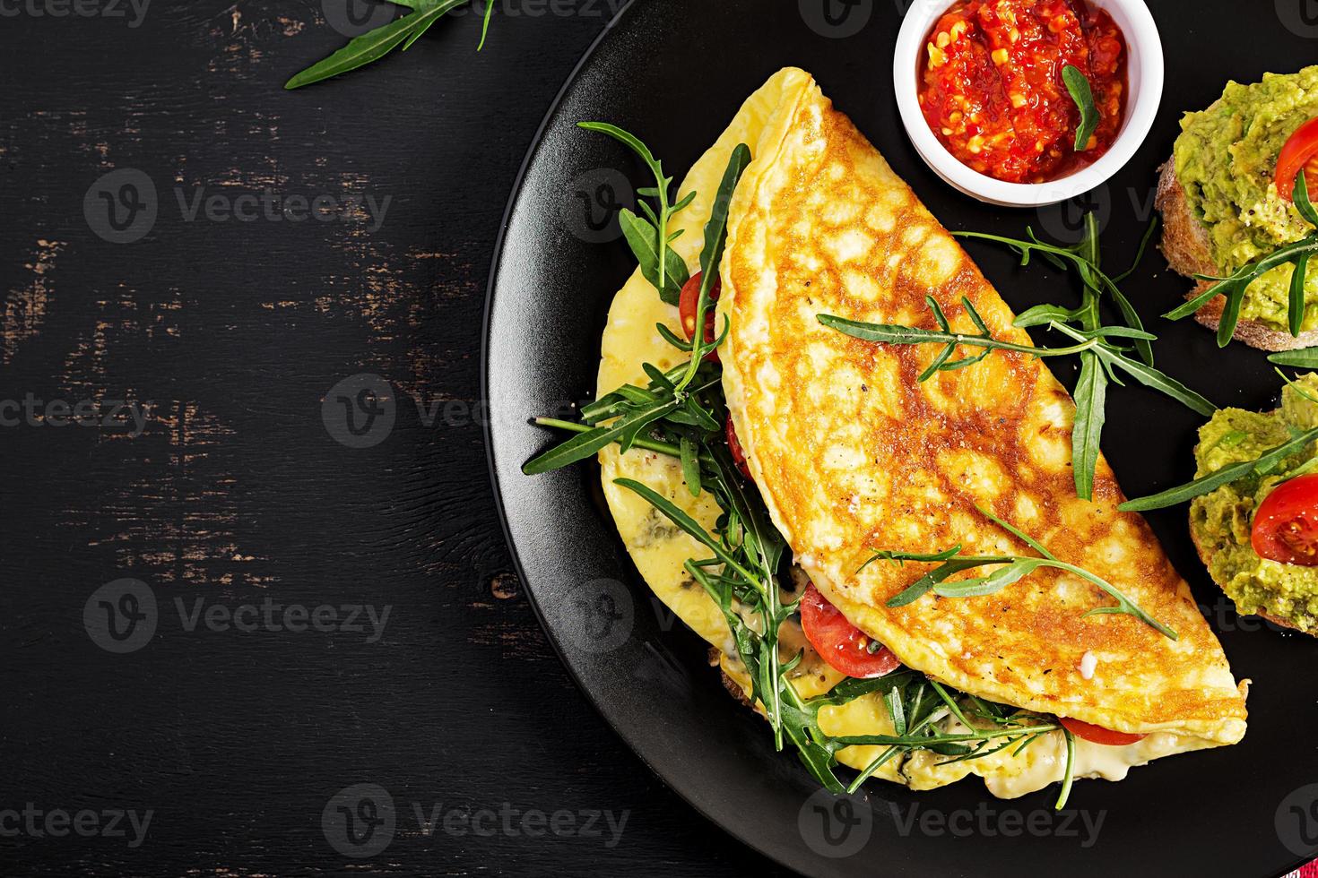 café da manhã. omelete com tomates, queijo, verde Rúcula e Torradas com abacate creme em Preto placa. fritada - italiano omelete. topo Visão foto