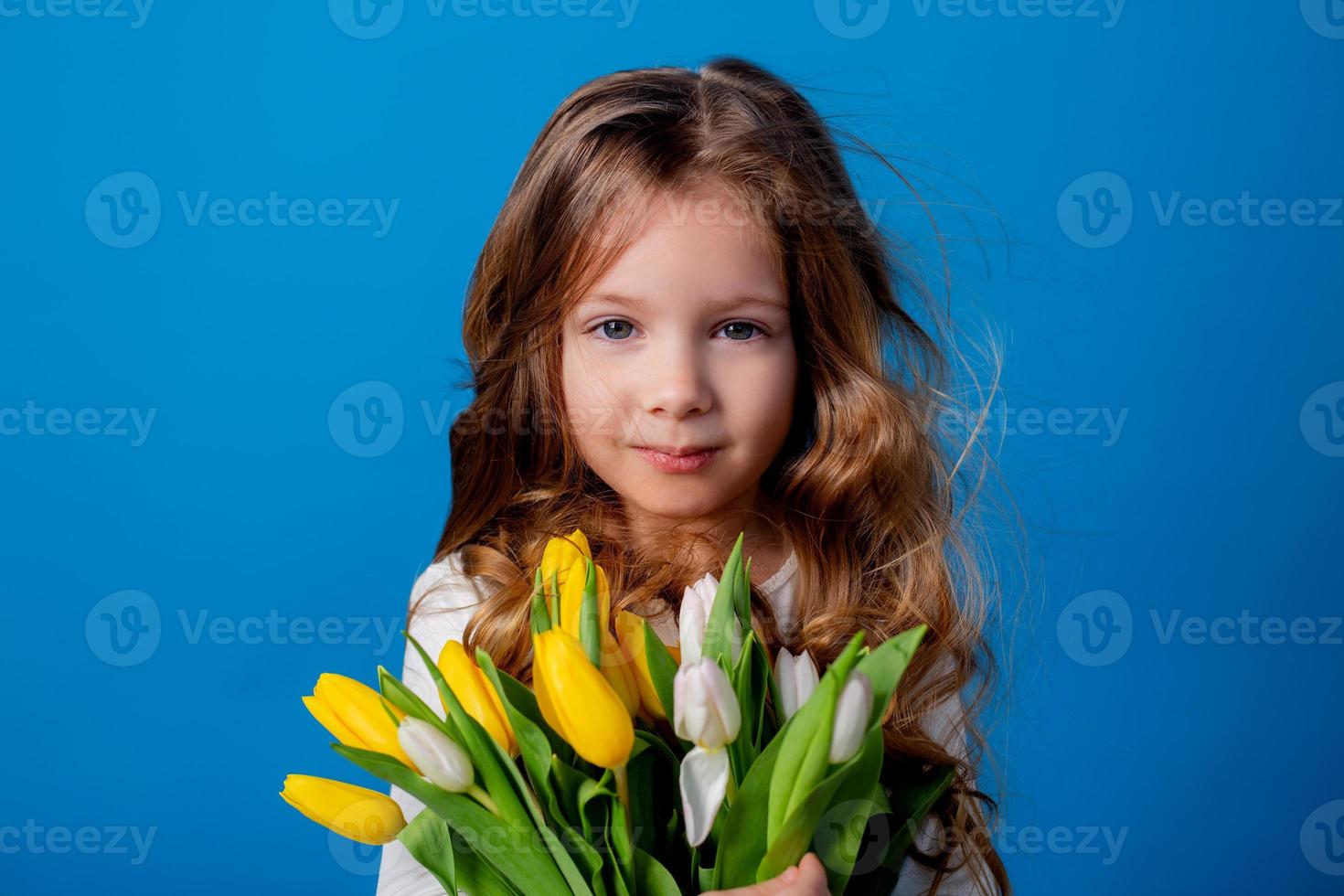 retrato do uma encantador sorridente pequeno menina com uma ramalhete do tulipas dentro dela mãos. estilo de vida. fresco flores internacional mulheres dia. espaço para texto. Alto qualidade foto