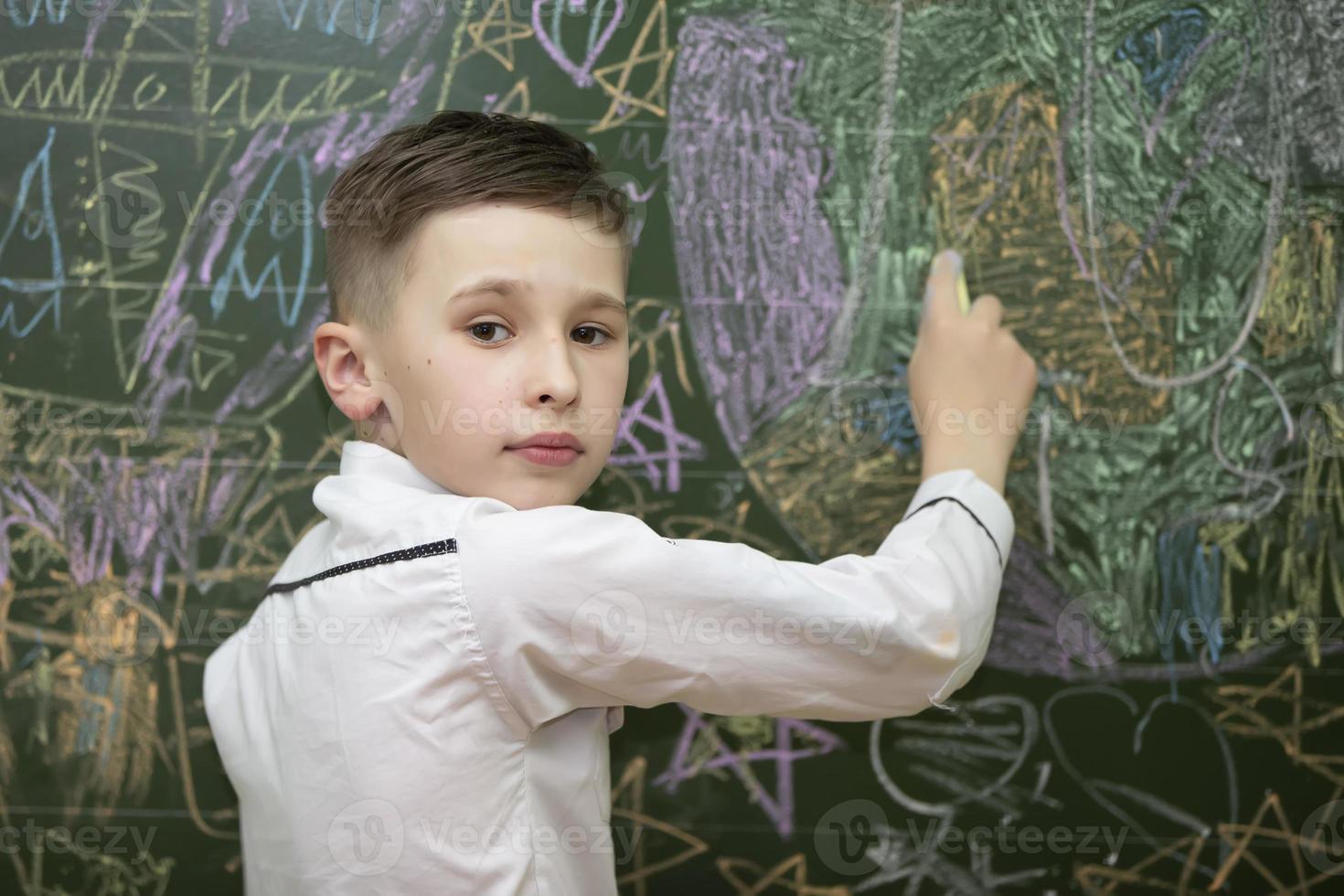 a estudante às a quadro-negro desenha com giz. meio escola idade. a Garoto é dentro a sala de aula. foto