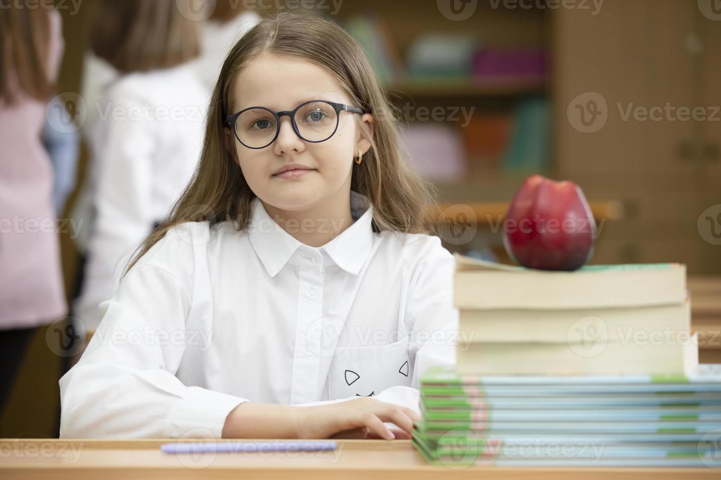 estudante dentro óculos às a escrivaninha. menina dentro a Sala de aula com livros e a maçã. secundário escola. costas para escola. foto