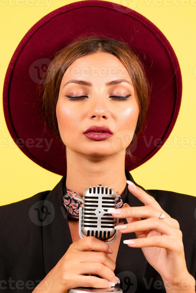 menina dentro uma Preto terno em uma amarelo fundo canta dentro uma retro microfone, retrato, música foto