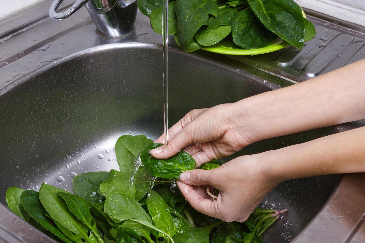 masculino mãos lavar espinafre. a Principal ingrediente para saboroso salada. espinafre folhas lavado dentro afundar. refeição preparação conceito foto