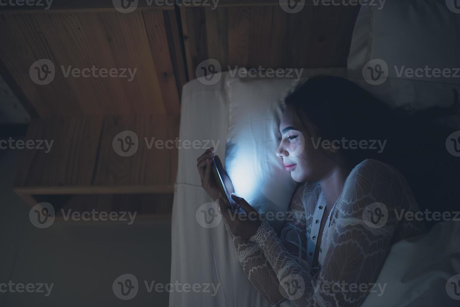 mulher asiática jogando no smartphone na cama à noite, tailândia, viciado em mídia social foto