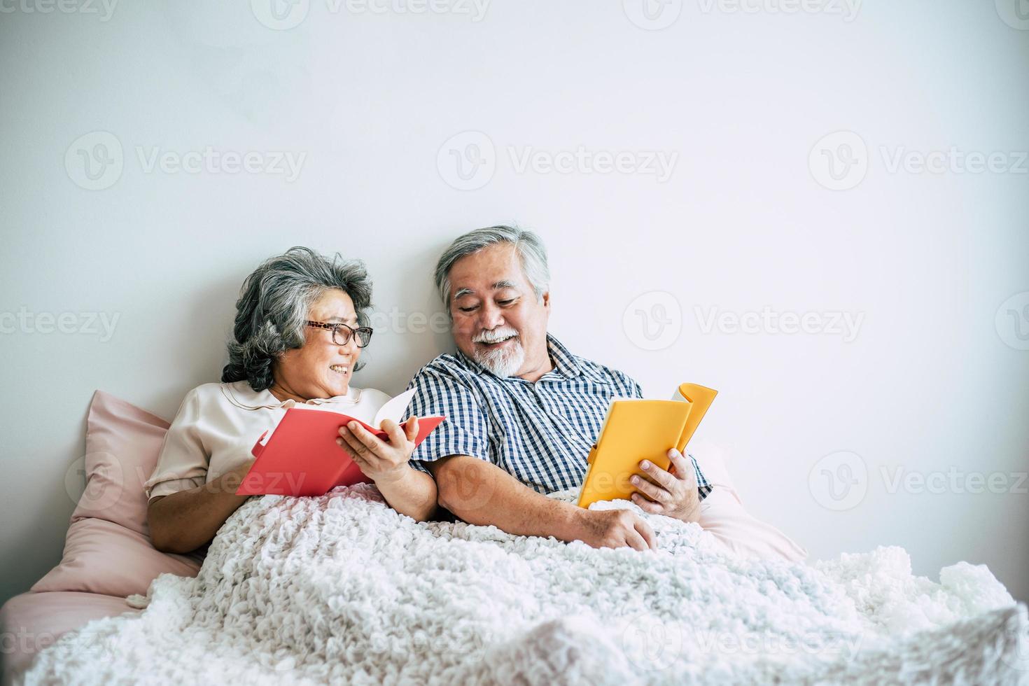 casal de idosos deitado na cama lendo um livro foto