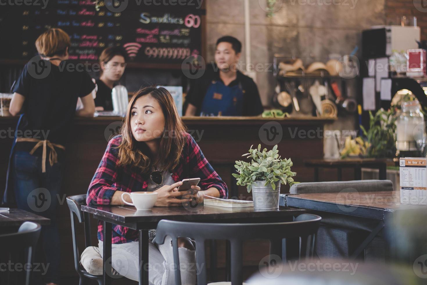 retrato de mulher jovem hippie usando telefone celular enquanto está sentado na mesa da cafeteria foto