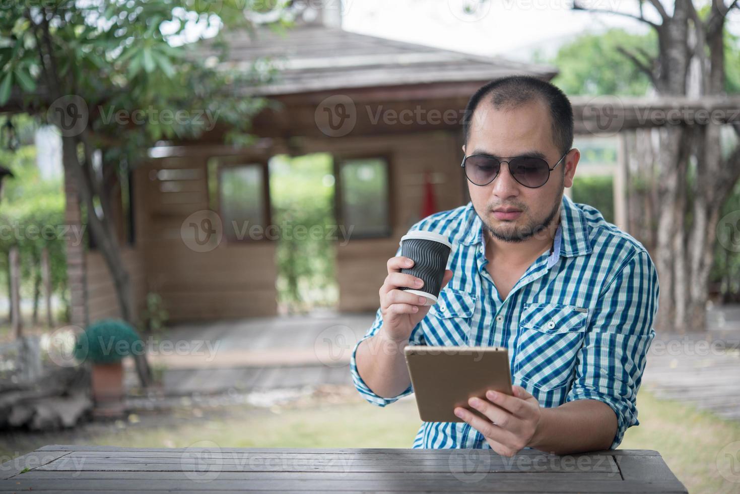 jovem sentado ao ar livre em uma mesa de madeira e relaxando com um tablet foto