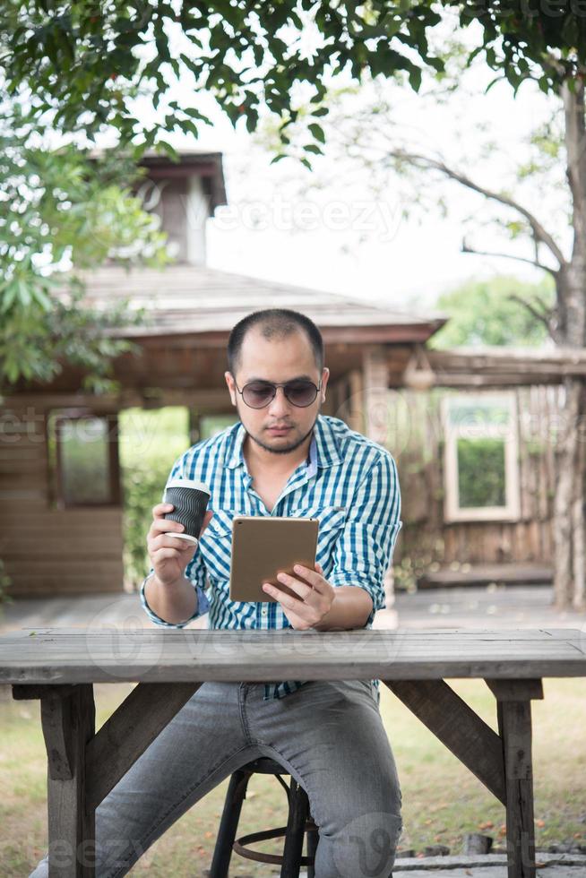 jovem sentado ao ar livre em uma mesa de madeira e relaxando com um tablet foto