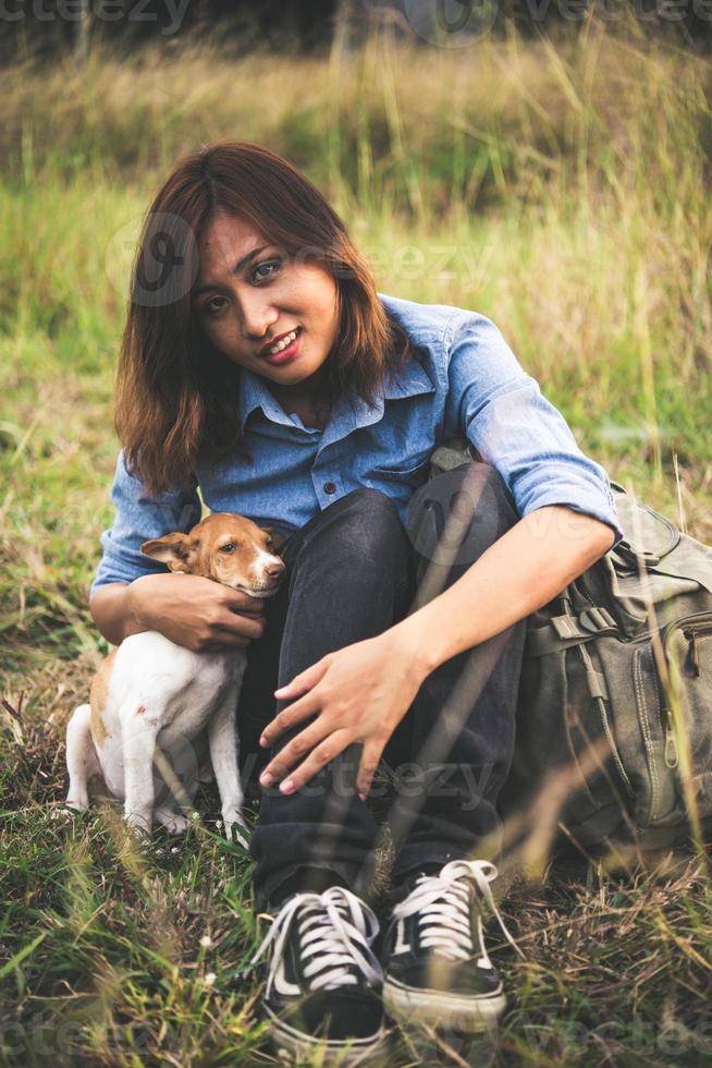 jovem sentada na grama com seu cachorrinho durante o pôr do sol foto