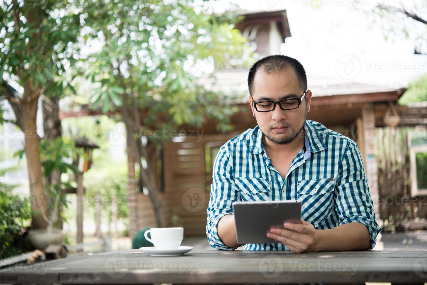 empresário trabalha em tablet enquanto está sentado à mesa de madeira em casa foto