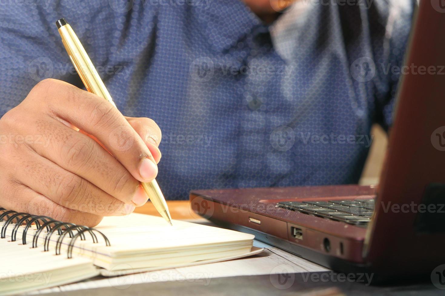 feche a mão do homem escrevendo em um caderno foto