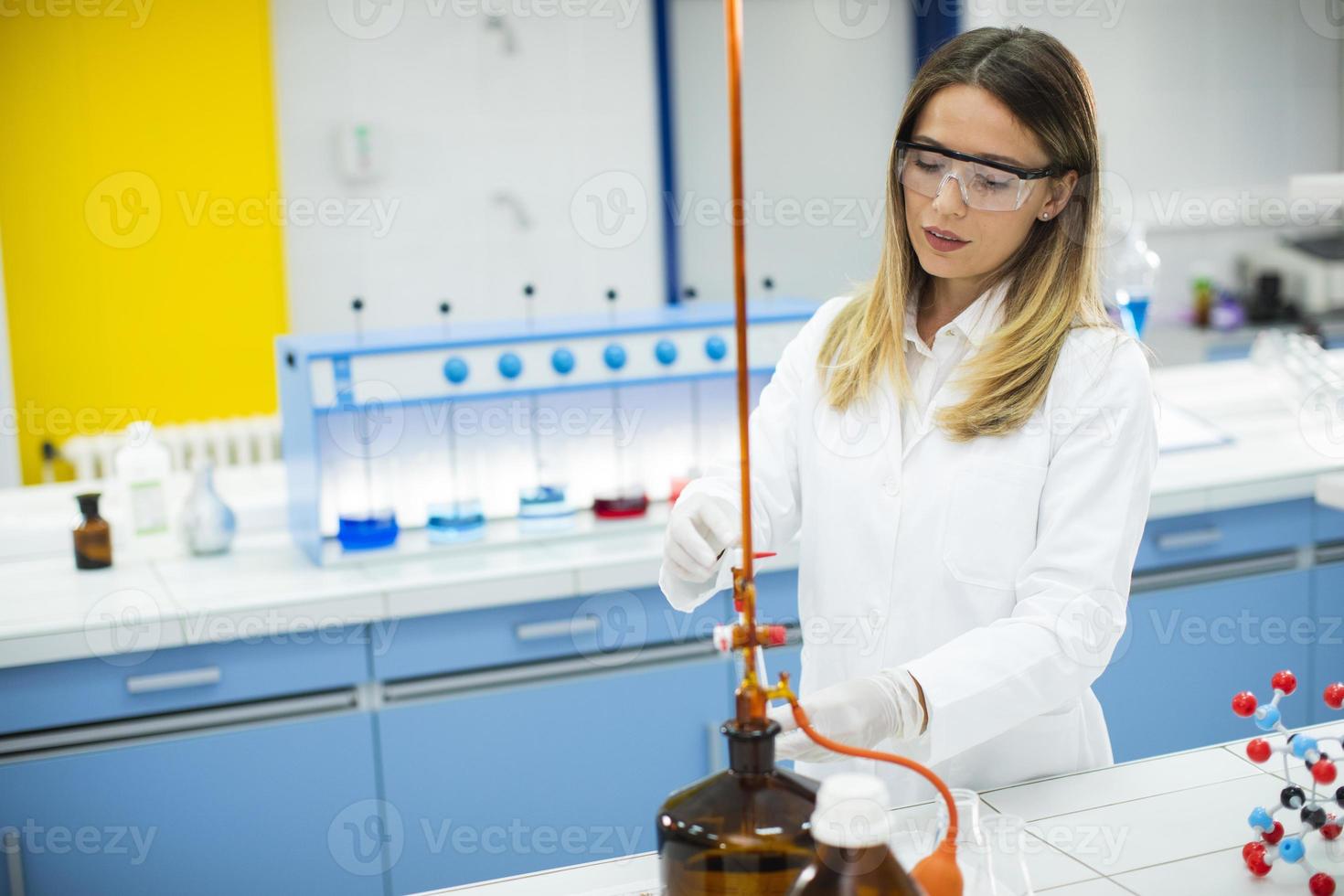 pesquisadora em roupas de trabalho de proteção em pé no laboratório e analisando frasco com amostra de líquido foto