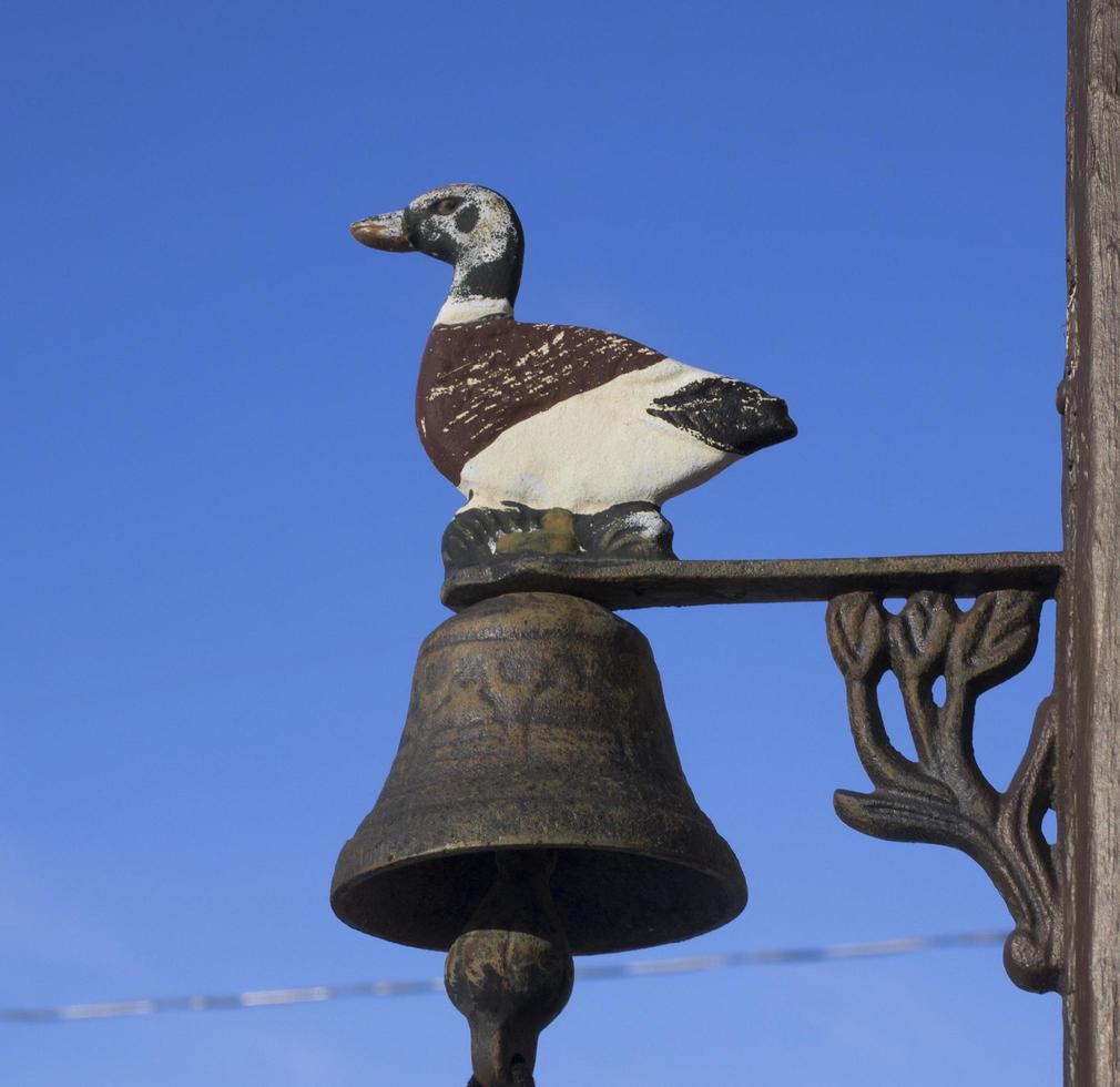 estátua de metal de um pato e um sino e um céu azul claro foto