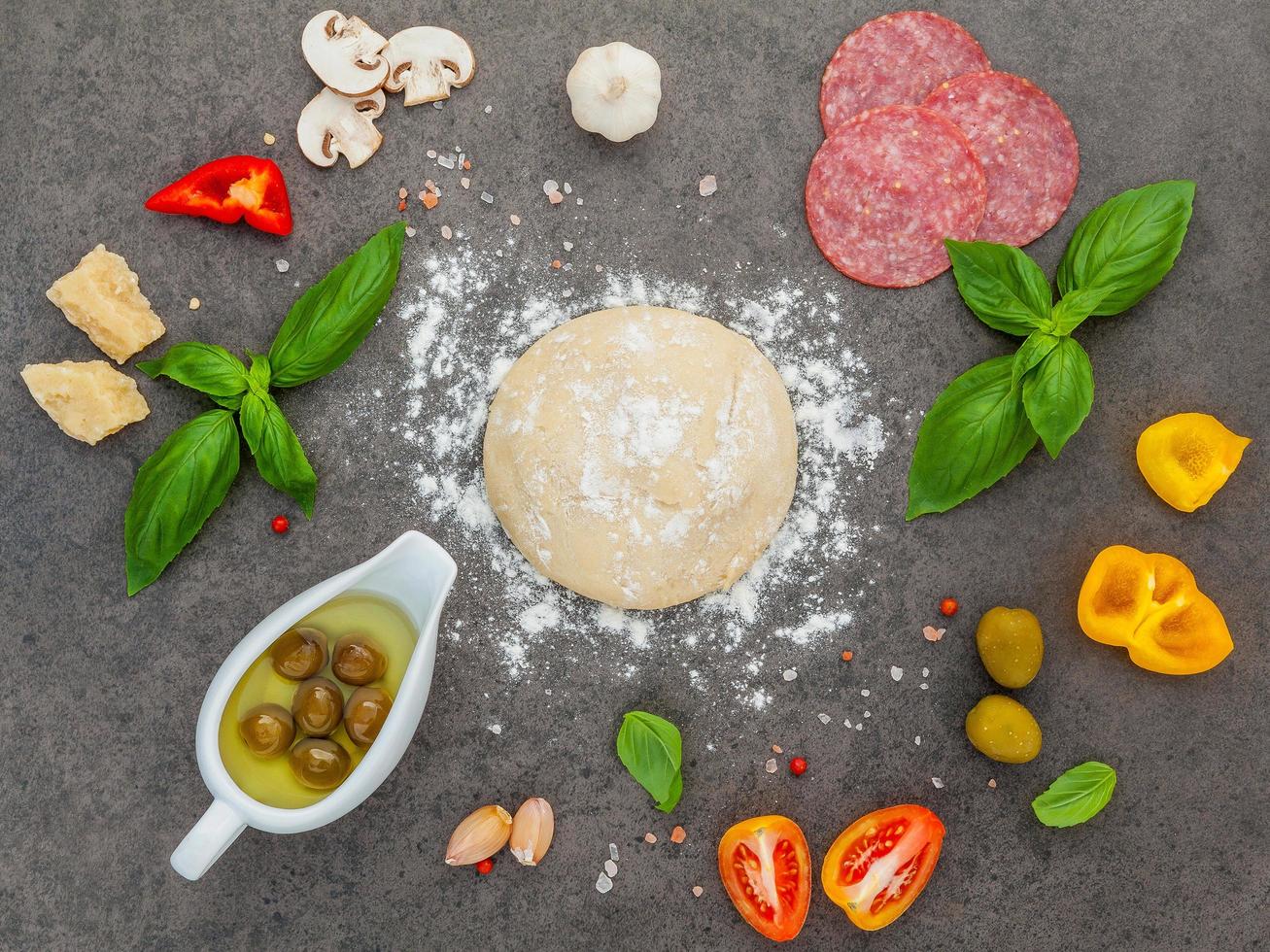 massa de pizza e ingredientes em um fundo escuro foto