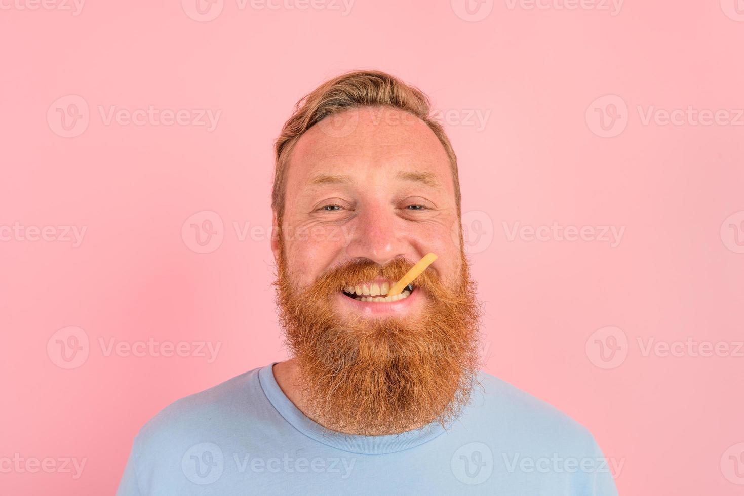 feliz homem com barba e tatuagens come frito batatas foto