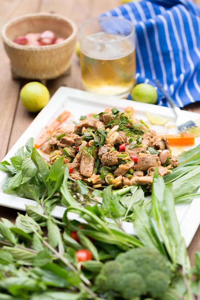 Salada de porco grelhado quente e picante em prato branco na mesa de madeira foto