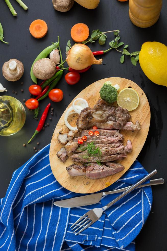 bife grelhado e guarnições na tábua de madeira com cebola, pimenta, tomate, feijão verde e limão na mesa de madeira escura foto