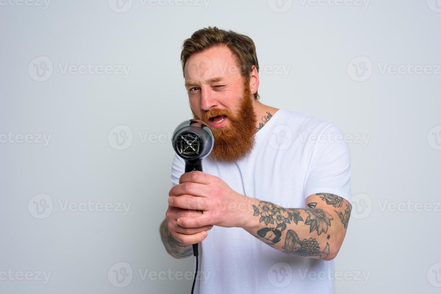 sério homem com barba jogar com cabelo secadoras uma revólver foto