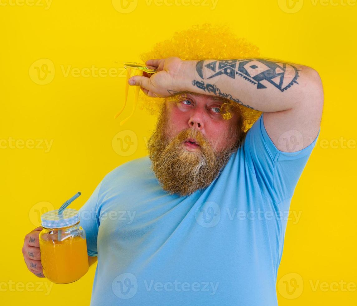 gordo cansado homem com peruca dentro cabeça e oculos de sol bebidas uma fruta suco foto