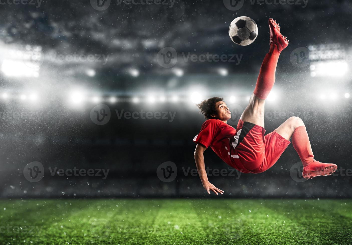 futebol atacante dentro vermelho uniforme exitos a bola com a acrobático pontapé dentro a ar às a estádio foto
