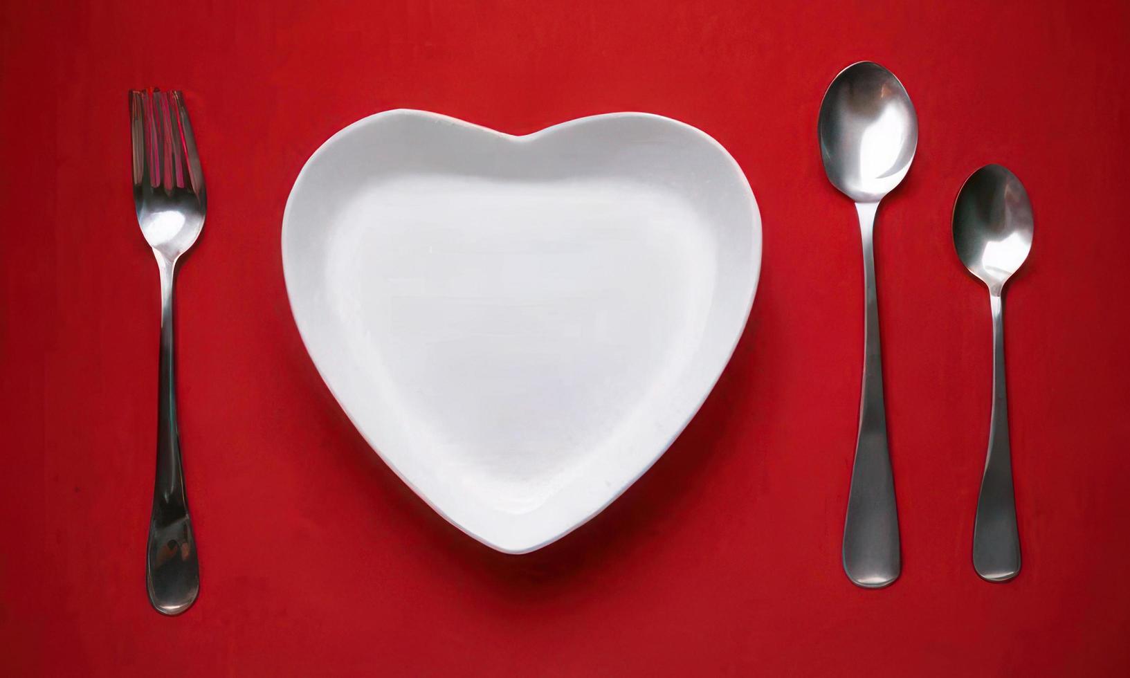 coração forma prato colher e garfo em vermelho fundo foto