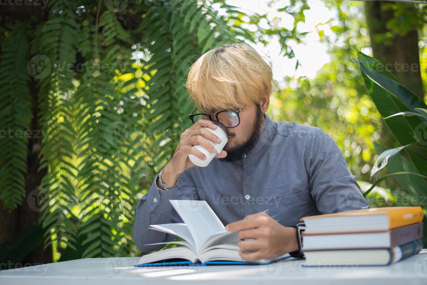 jovem hippie homem barba bebendo café enquanto lê livros no jardim doméstico com a natureza foto