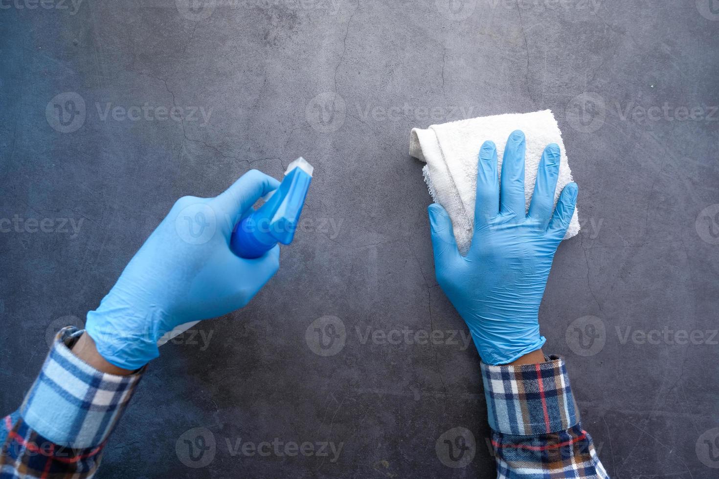 mãos com luvas de borracha azuis segurando um frasco de spray foto