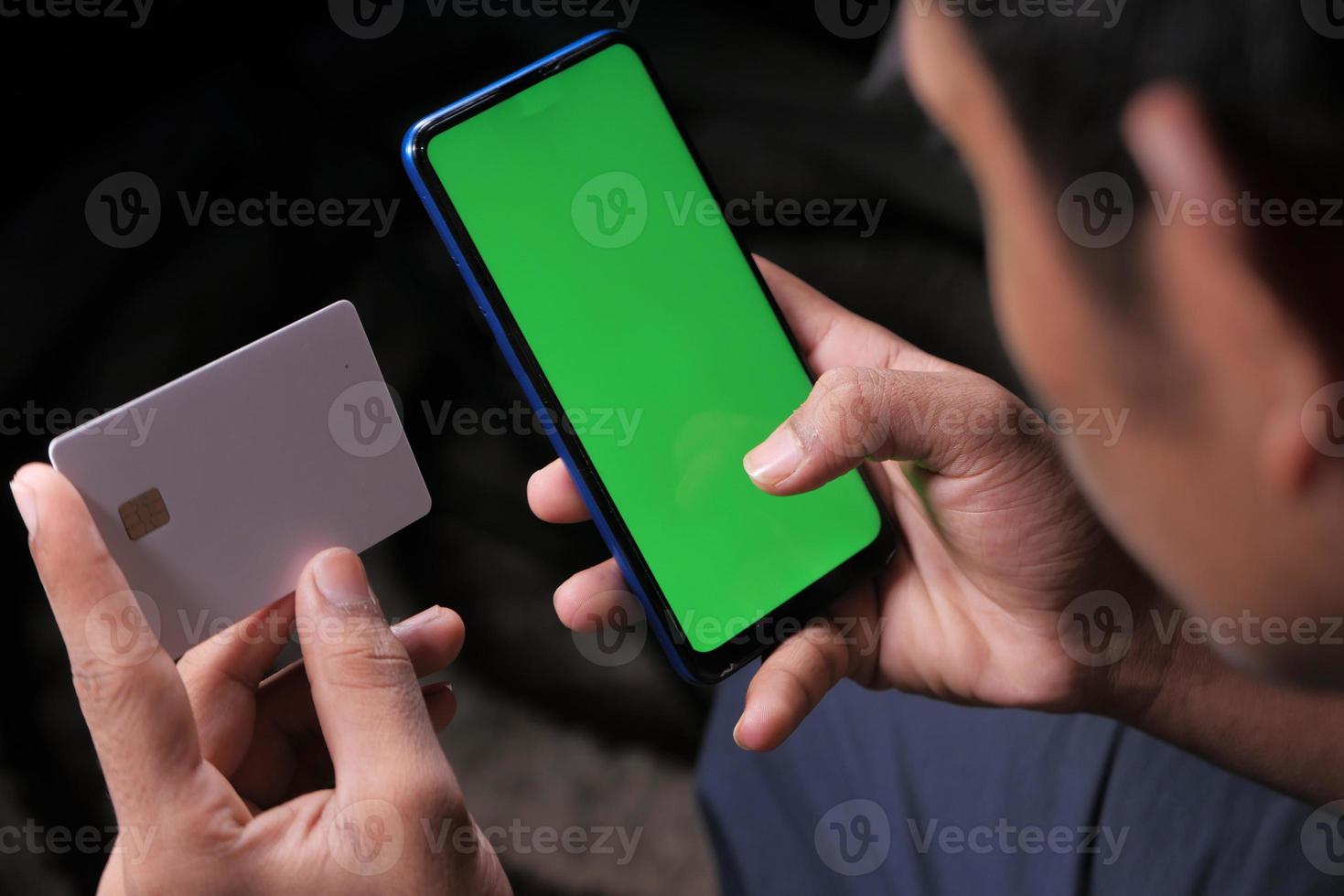 a mão de um homem segurando um cartão de crédito e usando um smartphone para fazer compras online foto