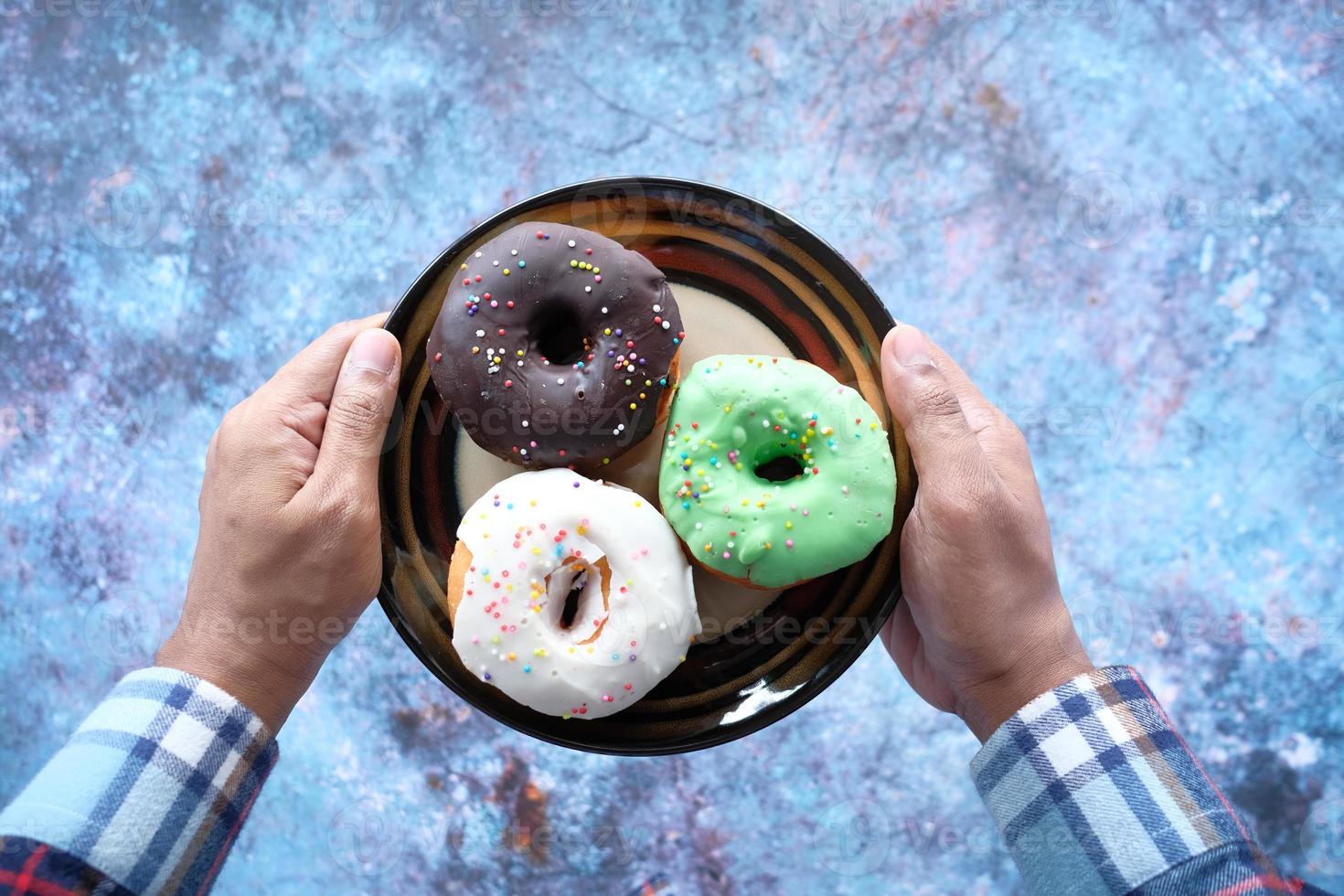 mão segurando um prato cheio de donuts vista de cima foto