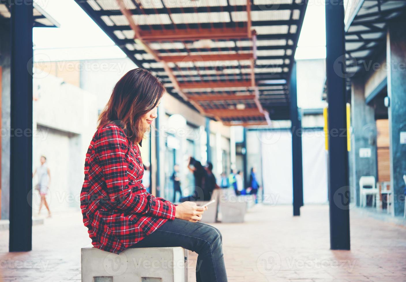 linda jovem hippie enviando mensagens de texto em seu smartphone, sentada em um banco foto