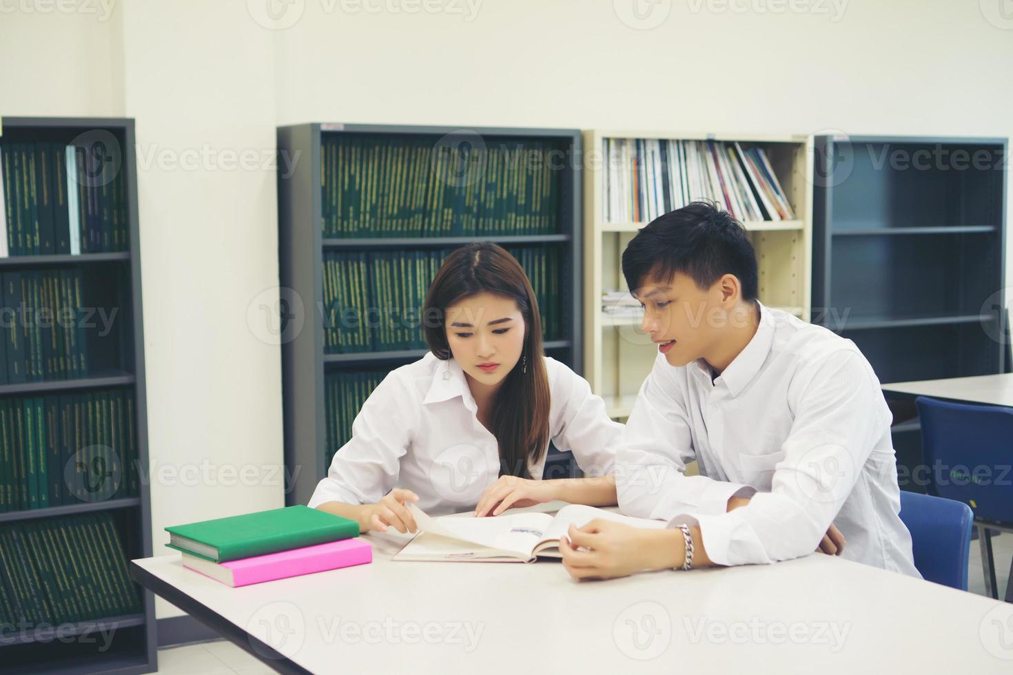 casal de jovens estudantes asiáticos na biblioteca lendo um livro juntos foto