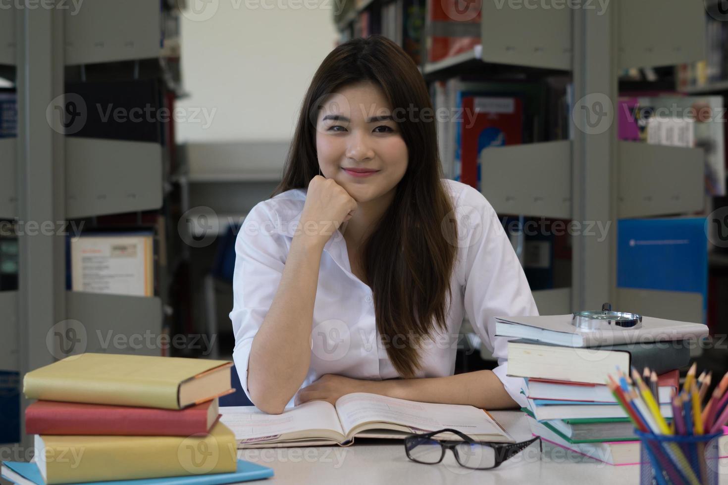 jovem estudante asiática sorrindo enquanto lê na biblioteca foto