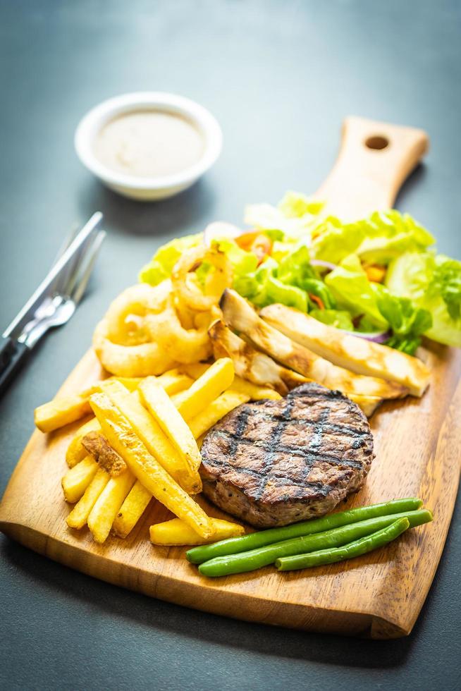 Bife grelhado com batata frita, molho e vegetais frescos foto